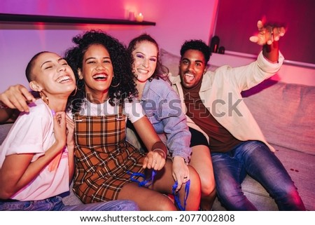 Group of friends having fun at a house party. Vibrant young people celebrating while sitting on a couch in bright neon light. Multicultural friends enjoying their weekend together. Stok fotoğraf © 