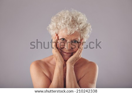 Portrait of senior caucasian woman touching her face against grey background. Feeling happy for her skin condition at old age.