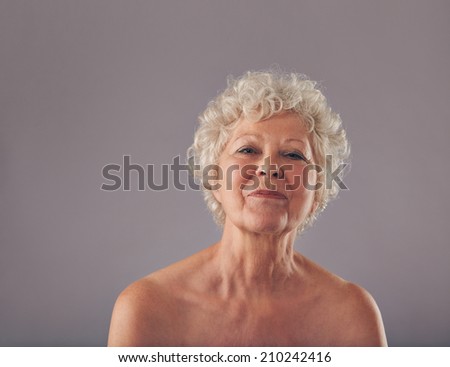 Portrait of confident old woman against grey background. Naked head and shoulders of senior female.