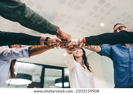 Modern businesspeople bringing their fists together while standing in a creative workplace. Diverse group of businesspeople smiling cheerfully while standing together in a huddle. 商業照片 © 