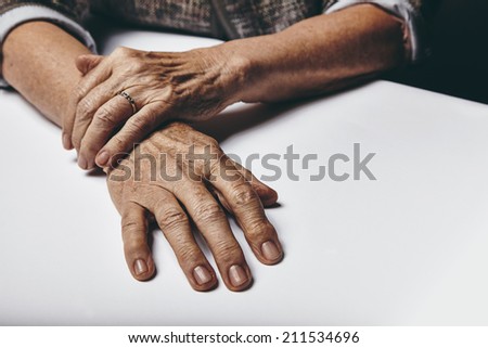 Close-up image of senior woman sitting by a table with focus on her hands. Old female hands on a desk.