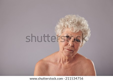 Portrait of a beautiful senior woman looking serious. Shirtless old lady looking sad with copy space on grey background.