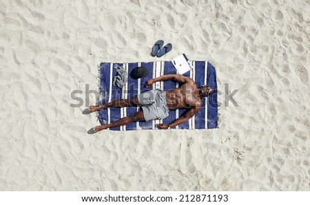 Top view of young man lying shirtless on a beach mat. African male model sunbathing.