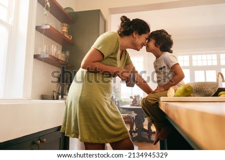 Affectionate mother touching noses with her young son in the kitchen. Cheerful mother and son looking at each other fondly. Loving single mother bonding with her son at home. Imagine de stoc © 