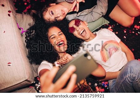 Vibrant selfies for vibrant people. Overhead view of three happy friends taking a selfie while lying on the floor at a house party. Group of cheerful female friends having fun together on the weekend. Stok fotoğraf © 