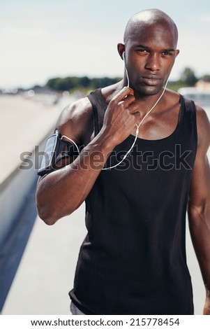 Portrait of fit young man outdoors listening to music on earphones. Healthy muscular man with arm band.