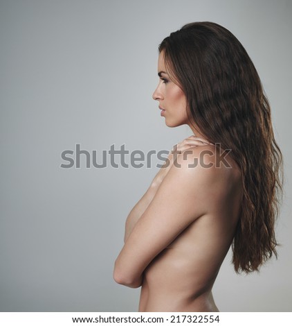 Side view of shirtless woman with beautiful curly long hair. Sexy female model on grey background