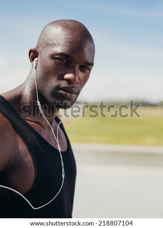Image of handsome young man wearing earphones looking at camera. African male model outdoors.