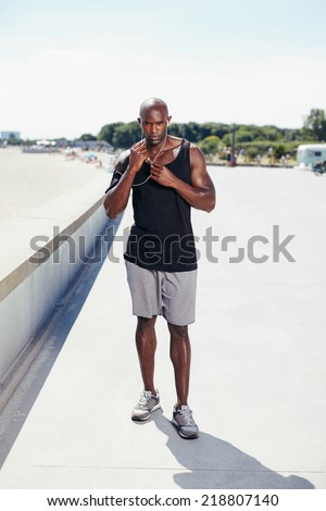 Full length portrait of fit young man outside listening to music on earphones. Muscular young male model.