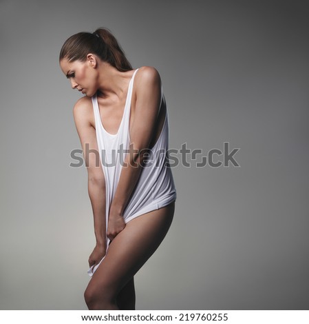 Studio shot of sexy female model posing on grey background. Sensual woman in tank top looking down.