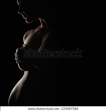 Low key portrait of curvy woman covering her breast with her hand. Naked woman against dark background.