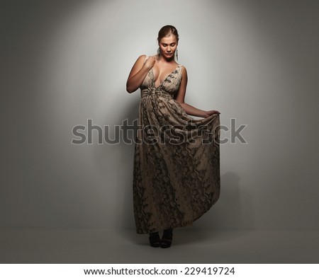 Pretty young lady in a evening dress standing on grey background. Plus size caucasian female model posing in beautiful evening gown.