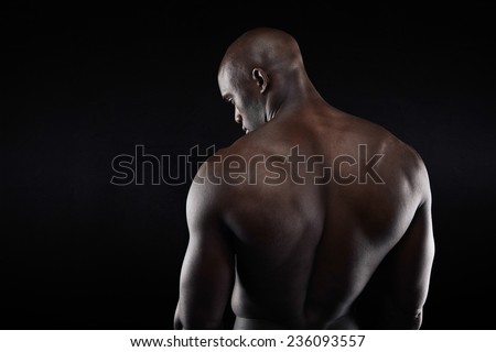 African muscular bodybuilder's back on black background. Shirtless fitness model with copyspace.