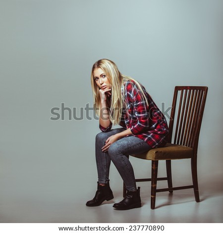 Studio shot of young woman in casual outfit sitting on chair looking at camera. Caucasian female model with copyspace.