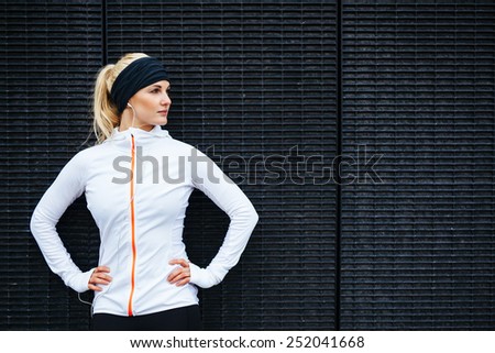 Portrait of determined young sports woman looking away while standing against a dark wall outdoors.