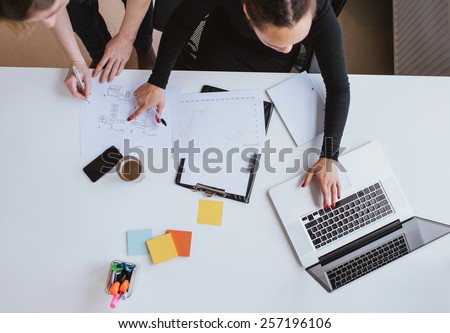 Business team working on a new plan with laptop. Top view of two young women executives working together with laptop and taking notes.