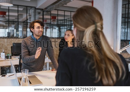 Young man explaining new business plan to coworkers during a meeting around a table in office.