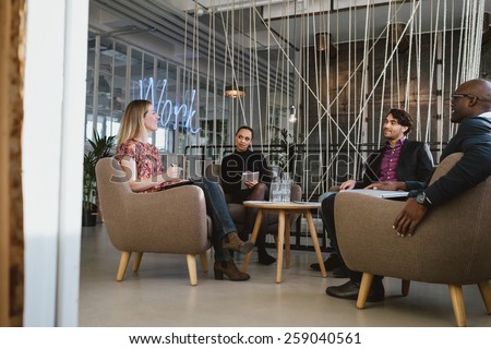 Happy young people sitting together in office discussing business. Office workers having a meeting in lobby. Diverse business people at startup.