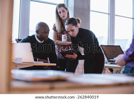 Female executive showing proposal on clipboard to her colleagues. Multiracial young people analyzing new business plan in office.