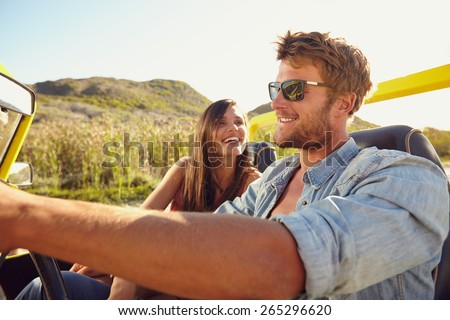 Cheerful young couple on a road trip enjoying the ride. Man driving beach buggy with woman smiling.
