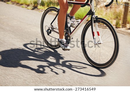 Low section image of woman riding bicycle on country road. Cropped image of female athlete cycling. Action shot of a racing cyclist.