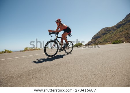 Image of young woman cycling on the country road. Fit female athlete riding down hill on bicycle. Woman doing cycling training.