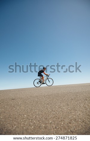 Image of male cyclist riding bicycle up hill. Athlete training for cycling event of a triathlon competition.