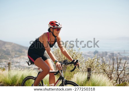 Outdoor shot of a female cyclist riding racing bicycle. Woman cycling on countryside road. Training for competition.