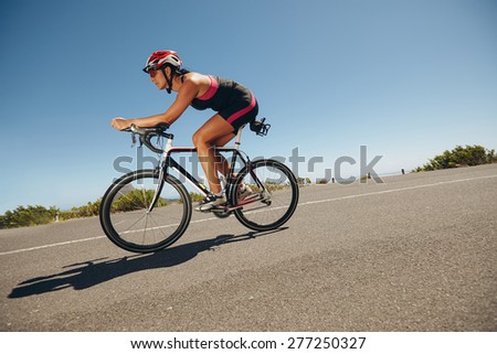 Female cyclist on a country road training for competition. Young woman riding bicycle down hill.