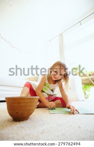 Portrait of preschool girl coloring picture on floor in her house. Young girl sitting on the floor painting a picture.