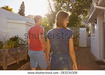 Rear view of young couple walking towards their house. Couple in backyard taking walk on a bright sunny day.