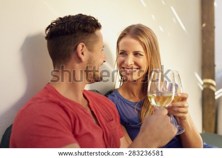 Happy young man and woman enjoying a glass of wine in their backyard. Couple toasting wine and looking at each other smiling.