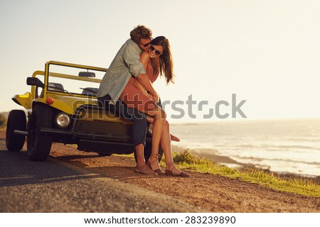 Romantic young couple sharing a special moment while outdoors. Young couple in love on a road trip. Couple embracing each other while sitting on hood of their car in nature.