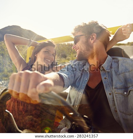 Happy young man and woman in a car enjoying a road trip on a summer day. Couple out on a drive in a open car.