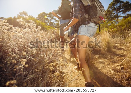 Cropped image of man and woman walking on country trail path. Young couple hiking on mountain on sunny day.