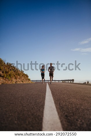 Two young people jogging on country road, low angle distant shot of runners running on open road on  a summer day.