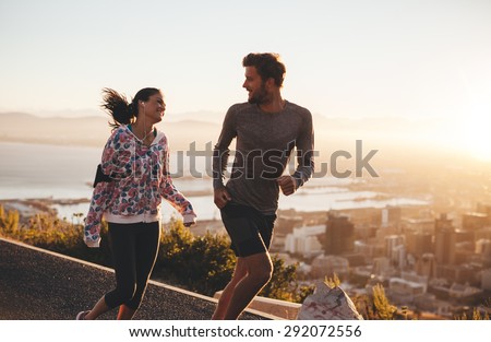 Young couple running together outdoors. Happy young man and woman jogging on country road during sunrise. Two people enjoying morning run.