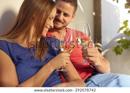 Happy young couple spending time in their backyard and enjoying a glass of wine. Smiling man and woman celebrating with wine, toasting wine glasses outdoors.