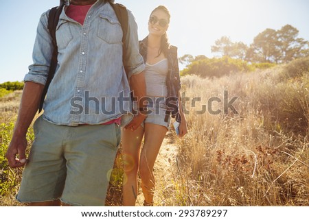 Image of young woman hiking in mountains with her boyfriend in front. Couple walking downhill on summer vacation.