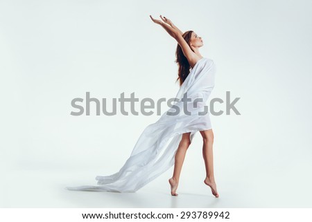 Side view portrait of a nude woman with hands raised in the studio. Attractive young woman with transparent fabric posing on white background.