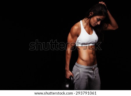 Fitness woman exercising crossfit holding kettle bell. Fitness instructor on black background. Female model with muscular fit and slim body.