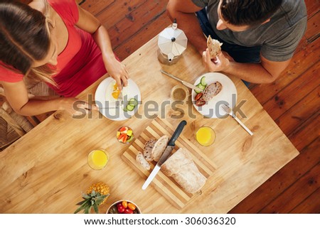 Top view of couple enjoying a healthy morning breakfast in kitchen at home. Breakfast table with loaf of bread, fruits, juice and coffee.