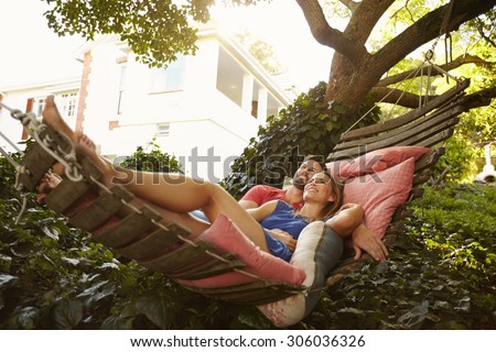 Portrait of an affectionate young couple lying on a hammock looking away smiling. Romantic young man and woman on garden hammock in backyard.