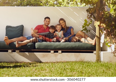 Portrait of happy young family sitting on patio smiling at camera. Couple with kids sitting on couch in their backyard.