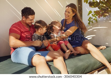 Shot of happy young family sitting together in patio. Couple with their children sitting on couch in backyard having fun.
