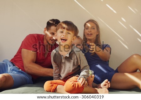 Happy little boy sitting on patio with his family at the back. Focus on little boy sitting in front with his parents and sister out of focus in background.