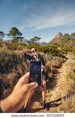 Young woman posing to mobile phone camera. Man hand holding a smart phone taking pictures on a young woman. Couple hiking in countryside on a summer day.
