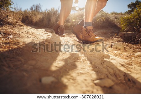 Hiking shoes in action on a country trail path. Close-up of male hikers shoes on dirt trail. Young people hiking on a sunny day.