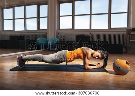 Young muscular woman doing core exercise on fitness mat in the gym. Fit female doing press-ups during the training in the health club.