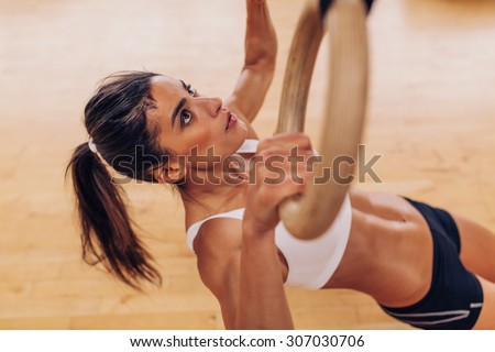 Portrait of young fit woman pulling up on gymnastic rings at gym. Muscular woman exercising with rings at health club.
